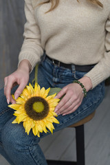 the girl has a jade bracelet, the girl is holding an artificial sunflower flower, the girl is sitting on a chair and holding a sunflower (vertically).