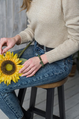 the girl has a jade bracelet, the girl is holding an artificial sunflower flower, the girl is sitting on a chair and holding a sunflower.