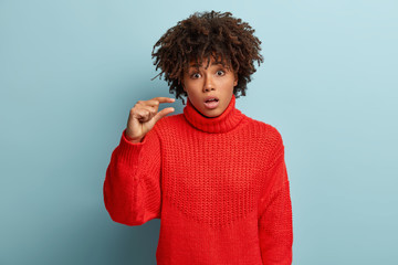 Omg, so small. Surprised African American woman disappointed as shapes tiny object, shows something...