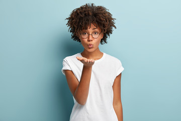 Photo of affectionate black lady sends air kiss, demonstrates good feelings, wears casual t shirt,...