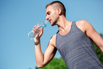 Healthy Lifestyle. Man practicing yoga outdoors standing with bottle dinking water thirsty bottom...