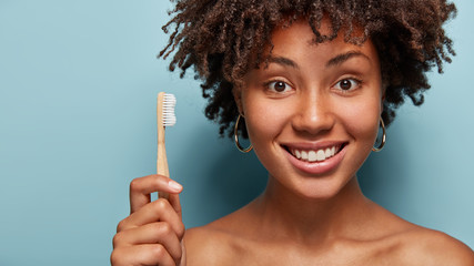 Oral hygiene concept. Optimistic healthy young woman with Afro haircut, holds wooden toothbrush in...