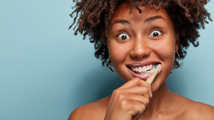 Cute short haired ethnic lady with happy expression, brushes teeth with toothbrush and paste, has...