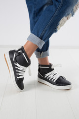 Studio Shot Of Female Legs In Stylish Black Leather Sneakers With White Shoelace, White Background Close Up