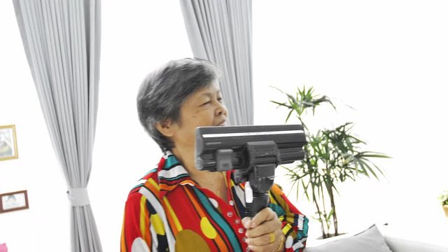 Asian Senior woman vacuuming floor at home. Dancing and singing with smile face. 4K Slow motion