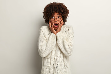 Dark skinned African American woman with crisp hair, keeps hands on cheeks, stares at camera with...