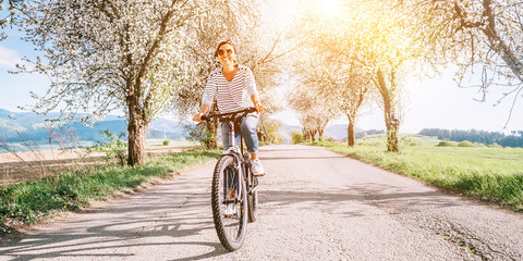 Happy smiling woman rides a bicycle on the country road under blossom trees. Spring is comming...