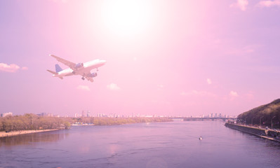 Airliner in the sky over the river. City and sunset.