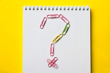 Notepad on yellow background with paper clips and question mark