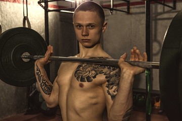 Fototapeta na wymiar Horizontal portrait of a young tattooes cross fit athlete doing the clean exercise with a barbell. Attractive sportsman working out shirtless. Power, training, agility, health concept