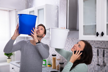 Woman Calling Plumber While Man Collecting Water From Ceiling