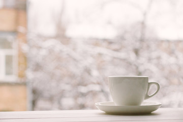 Obraz na płótnie Canvas White cup in window sill on a background of house and snowy weather.