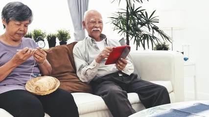 Asian senior man using tablet computer and Senior woman hand craft knitting wool at home. Old man with surprise  face  hand up. dolly shot. - Powered by Adobe