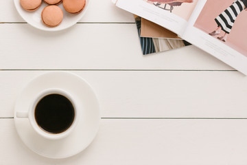 Cup of black coffee on a white wooden table with fashion magazine and macaroons. Author processing, film effect.