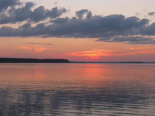 puesta del sol con nubes gris y cielo rosado, sobre lago 