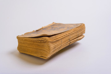 A closed old book with shabby pages lies on a white background.