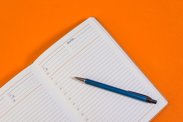 Open diary with a ballpoint pen on a sheet, on an orange background. 
