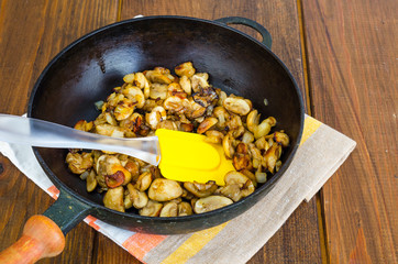 Black cast iron pan with fried mushroom slices on wooden background.