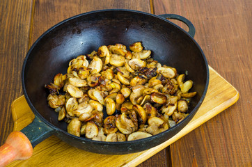 Black cast iron pan with fried mushroom slices on wooden background.