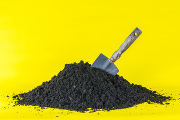 Shovel in Soil - Garden Trowel dug into Compost Heap - Yellow Background