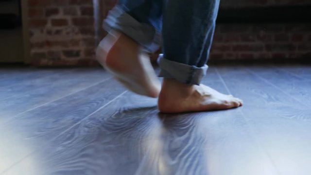 Barefoot guy legs in jeans trousers walking on parquet floor at home