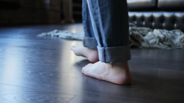 Barefoot girl legs in jeans trousers walking on parquet floor at home