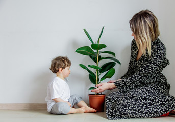 Young mother teaching a little toddler boy care with plant