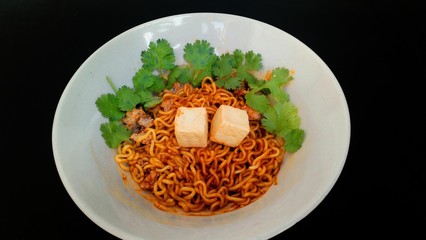 Thai spicy Yellow noodles , minced pork, tofu .. Sprinkle with coriander ... Put in a white dish. With a black background.