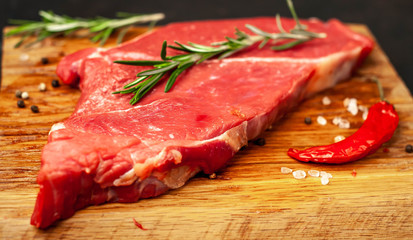 raw new york steak with ingredients on a cutting board. on the background of dark stone.