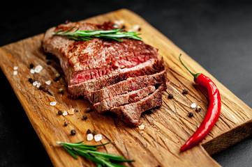 Ready to eat New York black angus steak with ingredients on a cutting board. Ready meal for dinner on a dark stone background.