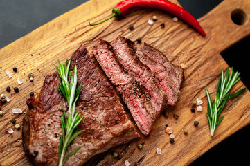 Ready to eat New York black angus steak with ingredients on a cutting board. Ready meal for dinner on a dark stone background.