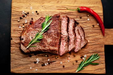 Ready to eat New York black angus steak with ingredients on a cutting board. Ready meal for dinner on a dark stone background.