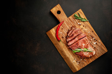 Ready-to-eat New York black angus steak with ingredients on a cutting board. Ready meal for dinner on a dark stone background.  with copy space
