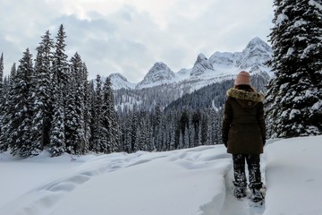Fototapeta na wymiar A young woman admiring the snowy views of Island Lake in Fernie, British Columbia, Canada. The majestic winter background is an absolutely beautiful place to go snowshoeing with fresh fallen snow.