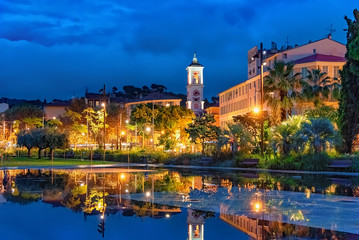 Place Massena in the city of Nice in evening lights with architecture reflected in water of the lovely fountain in France