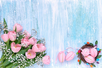 Easter background. Pink tulips and Easter eggs on blue background. Copy space, top view.