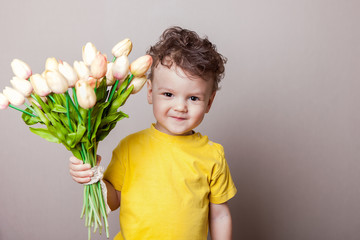 Smiling boy stretches forward bouquet of pink tulips isolated on white background