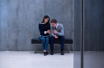 business couple using mobile phone while sitting on the bench