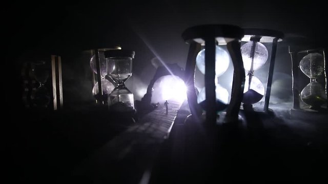 Time concept. Silhouette of a man standing between hourglasses with smoke and lights on a dark background. Surreal decorated picture