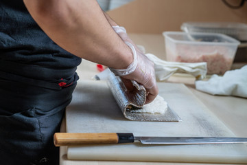 Cook hands making japanese sushi roll. Japanese chef at work preparing delicious sushi roll with eel and avocado. Appetizing japanese food.