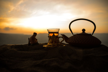Naklejka na ściany i meble Arabic tea in traditional glass and pot on desert at sunset. Eastern tea concept. Artwork decoration on sand with tea.