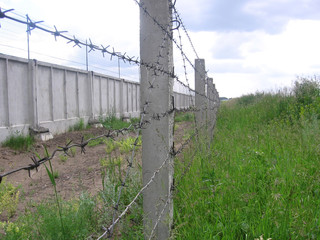 Obraz premium Green field of grass surrounded by concrete pillars, old barbed wire fence dangerous territory are out of bounds