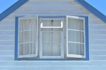 Roof facade of traditional wooden house painted in white and blue with horizontal cladding and multi pane window.