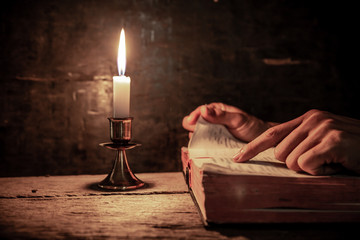 Close up hands of man readidng bible with light of candle on wooden table. christian concept.