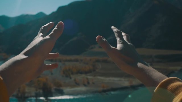 Girl looks at the sun through her hand. View of nature from the first person. A young girl looks at her hands, mountains and river in the background. Slow motion.