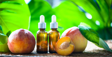Bottles with peach oil, fresh peach fruit whole and half on a natural tropical background. Homeopathic and herbal medicine.