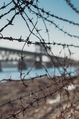 Automobile and railroad bridge behind barbed wire. Barbed Wire Fence and Bridge. Barb wire close up. Blur bridge behind barb wire.