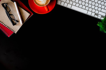 Office supplies with a laptop, smartphone, pen, tablet, notebook and coffee cup on a black background.