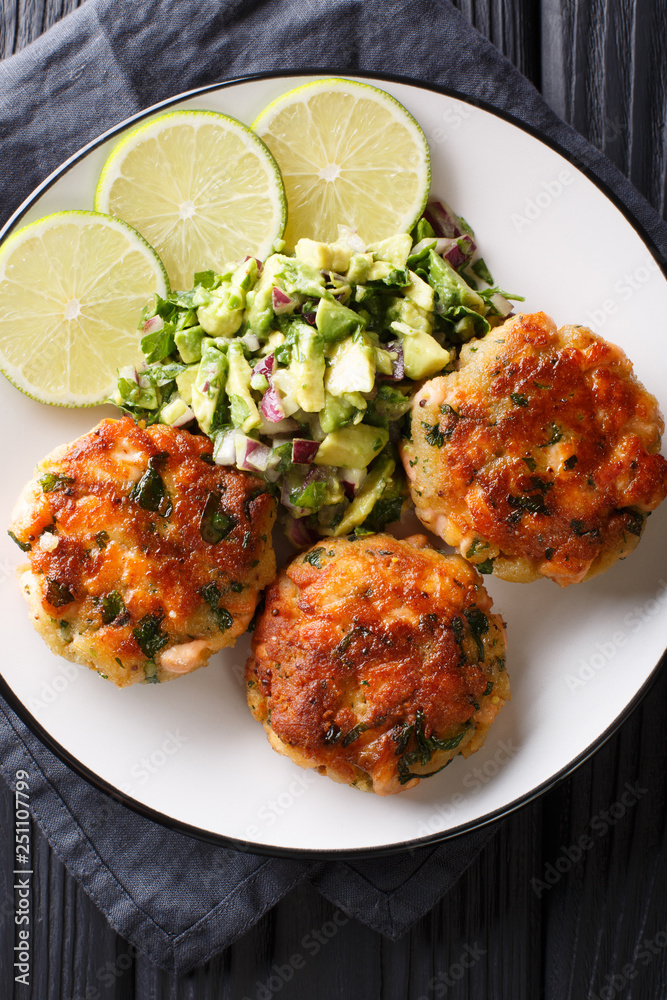 Wall mural Freshly made salmon burgers with avocado salsa and lime close-up on a plate. Vertical top view