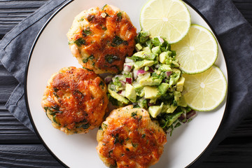 Freshly made salmon burgers with avocado salsa and lime close-up on a plate. horizontal top view